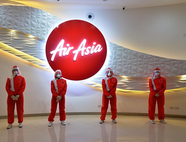 four people in red hazmat suits, with big AirAsia logo in the background