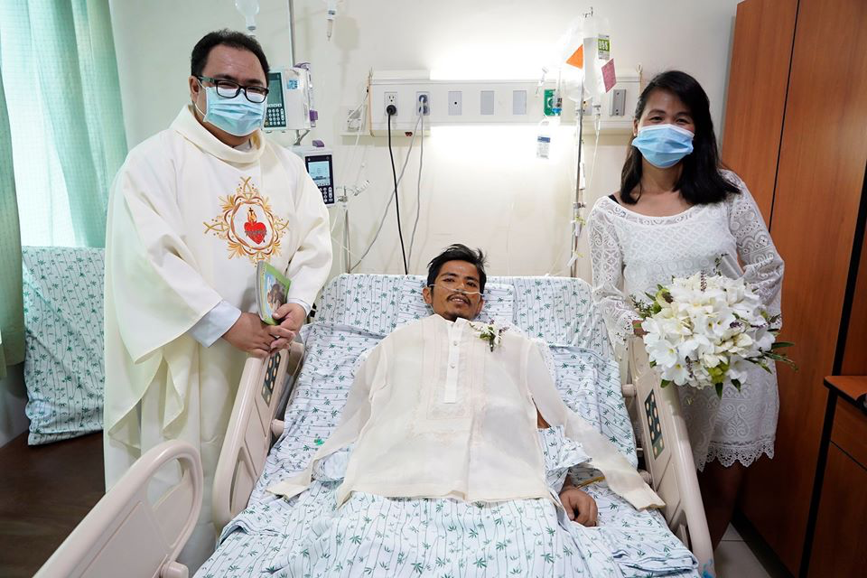 bride and priest stand beside groom in hospital bed
