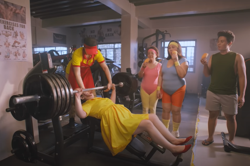 Julie's Bakeshop ad - Tita Julie weightlifting while the gym members eat the newly baked pandesal